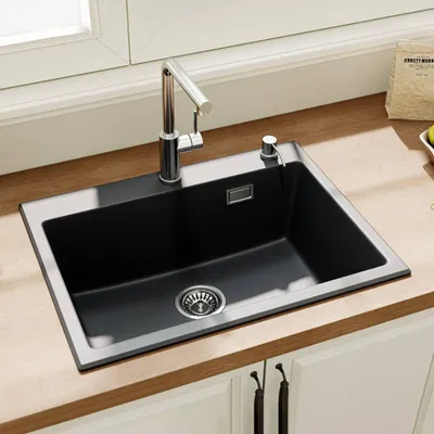 A black kitchen sink with a chrome faucet and soap dispenser is installed on a wooden countertop.
