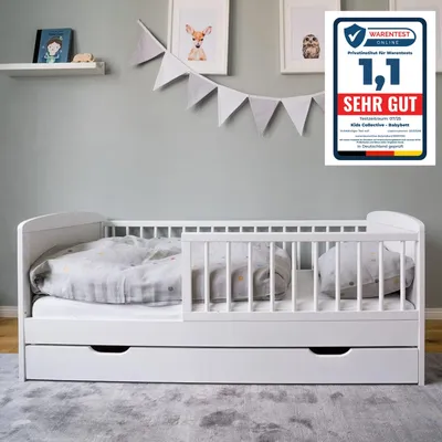 A white baby bed with a drawer underneath, set up in a child's room with decorations on the wall.