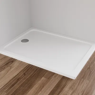 A white rectangular shower tray with a silver drain is shown in a corner against a light gray wall, with a wooden floor in the foreground.