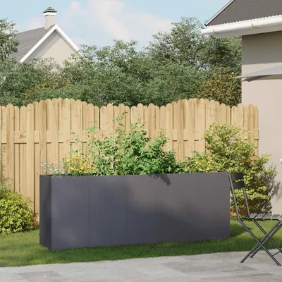 A modern, dark gray rectangular planter filled with green plants sits on a grassy lawn in front of a wooden fence. A house and trees are visible in the background.