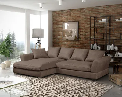 A modern living room with a large sectional sofa, a brick wall, and a large window with a view of trees.