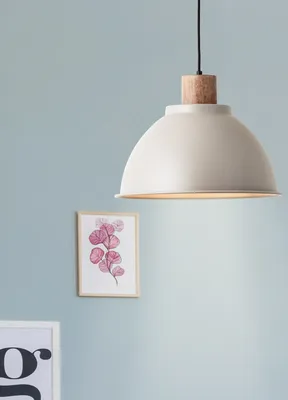 A taupe pendant light hangs in front of a light blue wall, with a framed picture of pink leaves to the left.