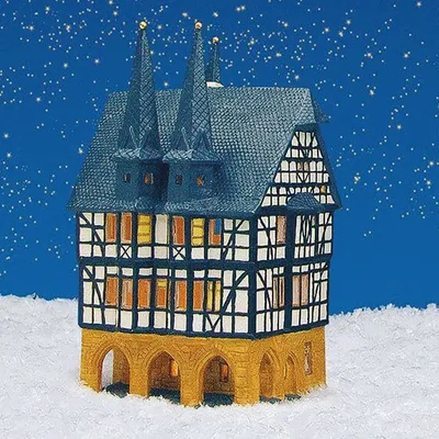A miniature half-timbered building, resembling a town hall, sits in a snowy landscape under a starry night sky.