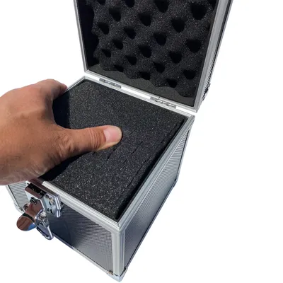 A hand is pressing down on the foam lining inside an open aluminum case.