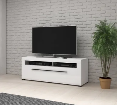 A modern white TV stand with a television on top, set against a white brick wall.