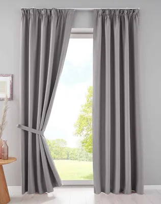 A pair of gray curtains are drawn back to reveal a window with a view of trees and greenery.