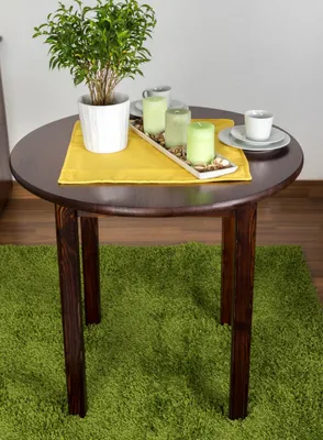 A round wooden dining table with a plant, candles, and a teacup on a green rug.