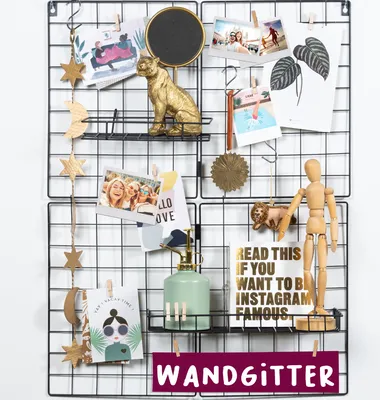 A black wire grid display board decorated with various items like photos, ornaments, and a small watering can.