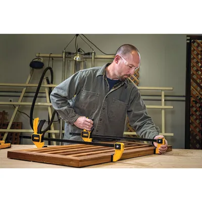 A man is using clamps to hold a wooden frame together in a workshop.