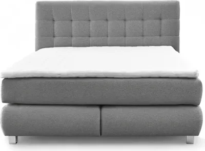 A studio shot of a gray boxspring bed with a white topper.