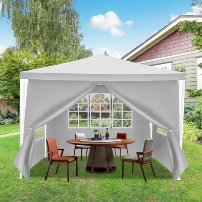 A white gazebo set up in a backyard with a table and chairs inside.
