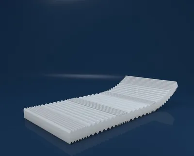A white mattress with a wavy, segmented surface is shown against a dark blue background.
