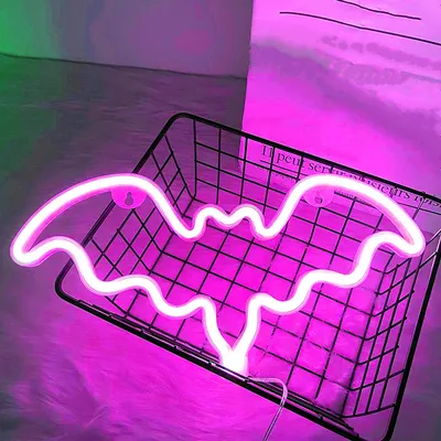 A neon bat light is displayed in a black wire basket, with a fuzzy white surface underneath and a pink and green gradient background.