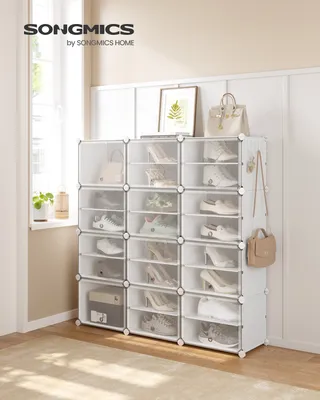 A white shoe rack with multiple compartments filled with shoes and bags, placed in a room with natural light coming from a window.
