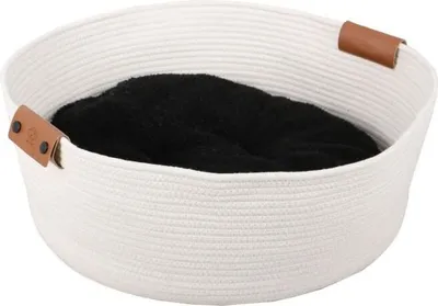 A white woven pet bed with a black cushion inside, featuring brown leather handles.