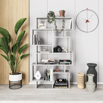 A modern living room with a tall, geometric bookshelf filled with books and decorative items, a large potted plant, and a clock on the wall.