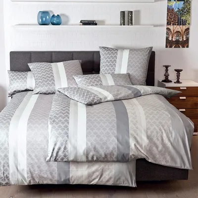 A neatly made bed with a grey headboard and a duvet cover set with a striped pattern in shades of grey and white.