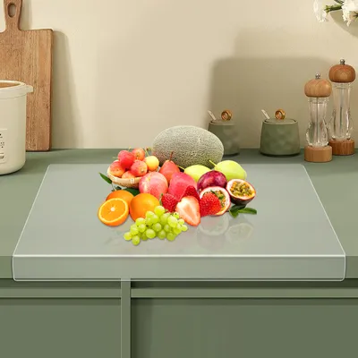 A collection of fruits is displayed on a clear cutting board placed on a kitchen counter.