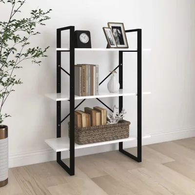 A white and black bookshelf with books, a clock, and picture frames on it, placed against a white wall and on a wooden floor.