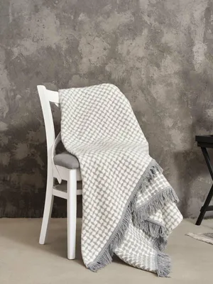A grey and white patterned blanket draped over a white chair against a textured grey wall.