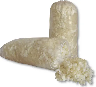 Two bags of shredded filling material, likely for pillows or cushions, are shown against a white background. One bag is lying horizontally in the foreground, with some material spilled out. The other bag stands vertically in the background.
