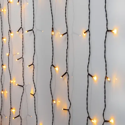 A close-up view of multiple strands of LED string lights hanging vertically against a light gray wall.