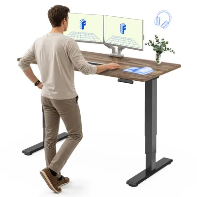 A man is standing at a height-adjustable desk with two monitors.