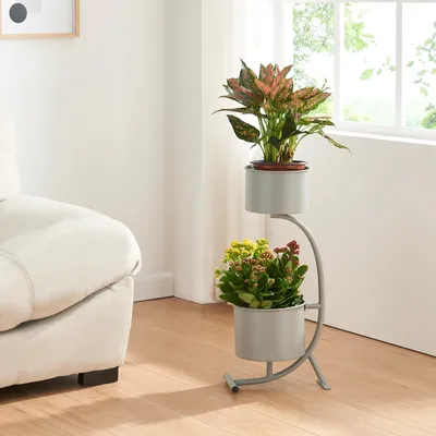 A two-tiered plant stand with two potted plants is placed next to a sofa in a room with a window.