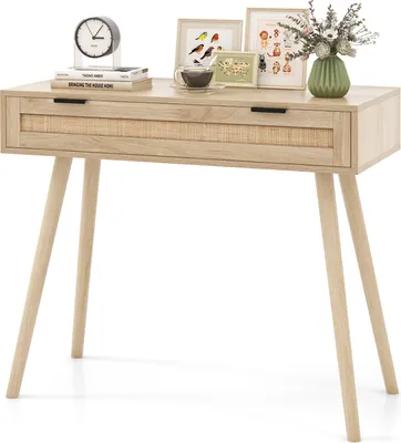A light wood console table with a rattan drawer front, decorated with framed pictures, a clock, and a vase of flowers.