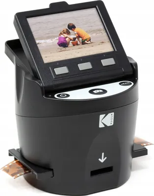 A Kodak film scanner is shown on a white background. The scanner has a screen displaying a photo of two children on a beach.