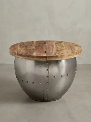 Freigestellter Industrial Couchtisch mit runder Mangoholzplatte und silbernem Metallkorpus mit Nieten, Frontalansicht auf weißem Hintergrund._#sku_BARWL6.310#