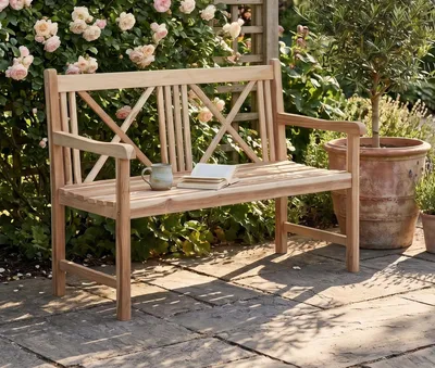 Gartenbank Malmö 2-sitzig aus Teak mit Armlehnen in Natur-Holzton, Gesamtansicht im begrünten Garten stehend.