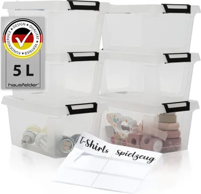 A stack of clear plastic storage boxes with black lids and clips, some containing small items. A label with German text and a German flag logo is visible on the left.