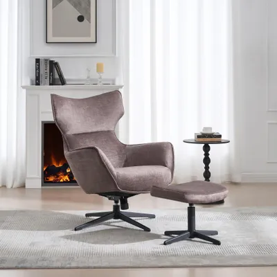 A taupe velvet armchair and ottoman are placed in a living room setting with a fireplace and curtains in the background.