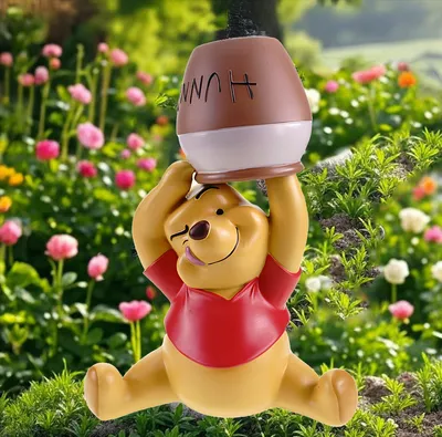 A Winnie the Pooh figurine holding a honey pot, set against a backdrop of flowers and greenery.