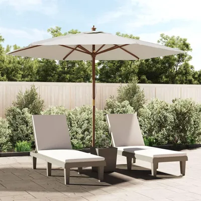 Two lounge chairs and a large umbrella are set up on a patio, surrounded by lush greenery and a wooden fence.
