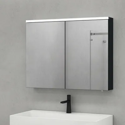 A bathroom medicine cabinet with mirrored doors is mounted on a gray wall above a white sink with a black faucet.
