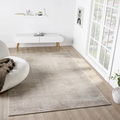A rug is placed on a wooden floor in a modern living room, next to a white armchair and a white console table. A large window is visible on the right.