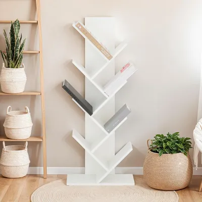 A white tree-shaped bookshelf filled with books, placed in a room with a ladder shelf and baskets.