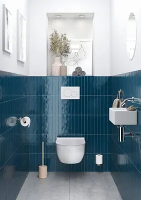 A modern bathroom with blue tiled walls, a white toilet, and a small sink.