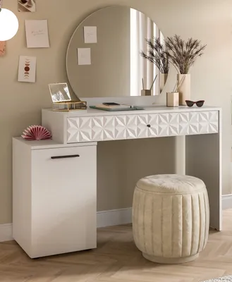 A white vanity table with a round mirror, a stool, and a side cabinet, decorated with framed pictures and a vase of dried flowers.
