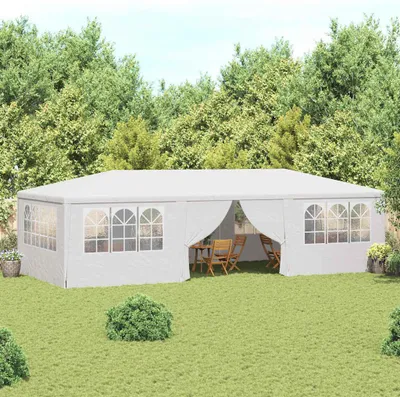 A white party tent set up in a grassy backyard with trees in the background.