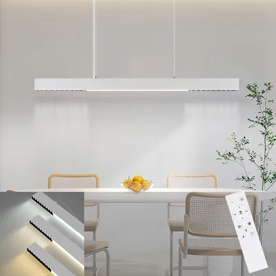 A modern white LED pendant light hangs above a dining table with chairs and a bowl of fruit.