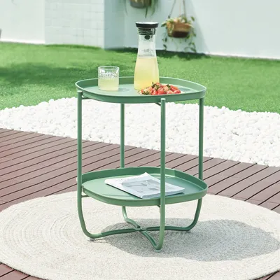 A green side table with drinks and fruit on it, placed on a patio.