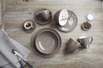 A collection of taupe ceramic dishes and cups arranged on a wooden surface, with cutlery on a grey napkin.