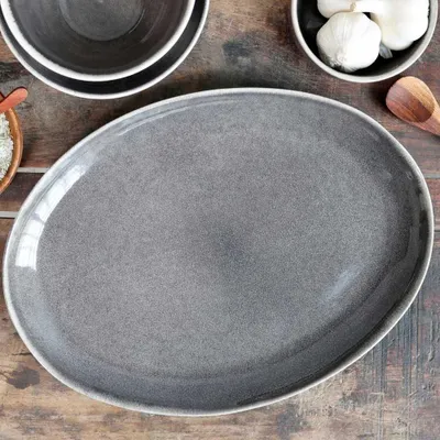 A gray oval serving platter on a wooden table, with bowls of rice and garlic in the background.
