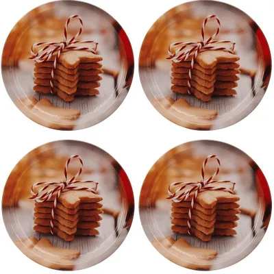 Four round plates, each featuring a stack of star-shaped cookies tied with red and white twine, set against a blurred background of wooden planks and warm lighting.