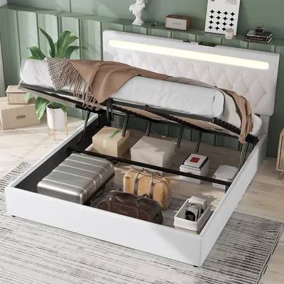 A white storage bed with its hydraulic lift mechanism open, revealing storage space filled with luggage and boxes. The bed has a tufted headboard with integrated LED lighting.