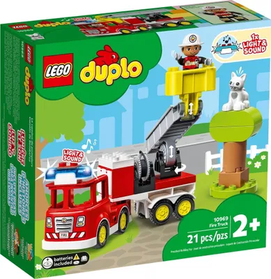 The image shows the packaging of a LEGO DUPLO fire truck set, with the toy fire truck and accessories depicted on a green and white background with cartoonish trees and a fence.