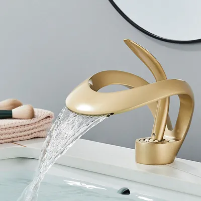 A close-up shot of a modern gold waterfall faucet in a bathroom sink, with water flowing.